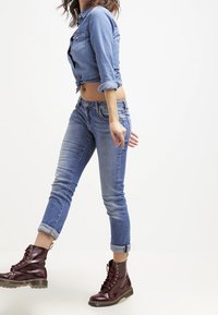 Světlomodrá džínová košile zavázaná v pase, kombinovaná s vyšisovanými modrými skinny džíny a vínovými kotníkovými botami na tkaničky s masivní podrážkou.