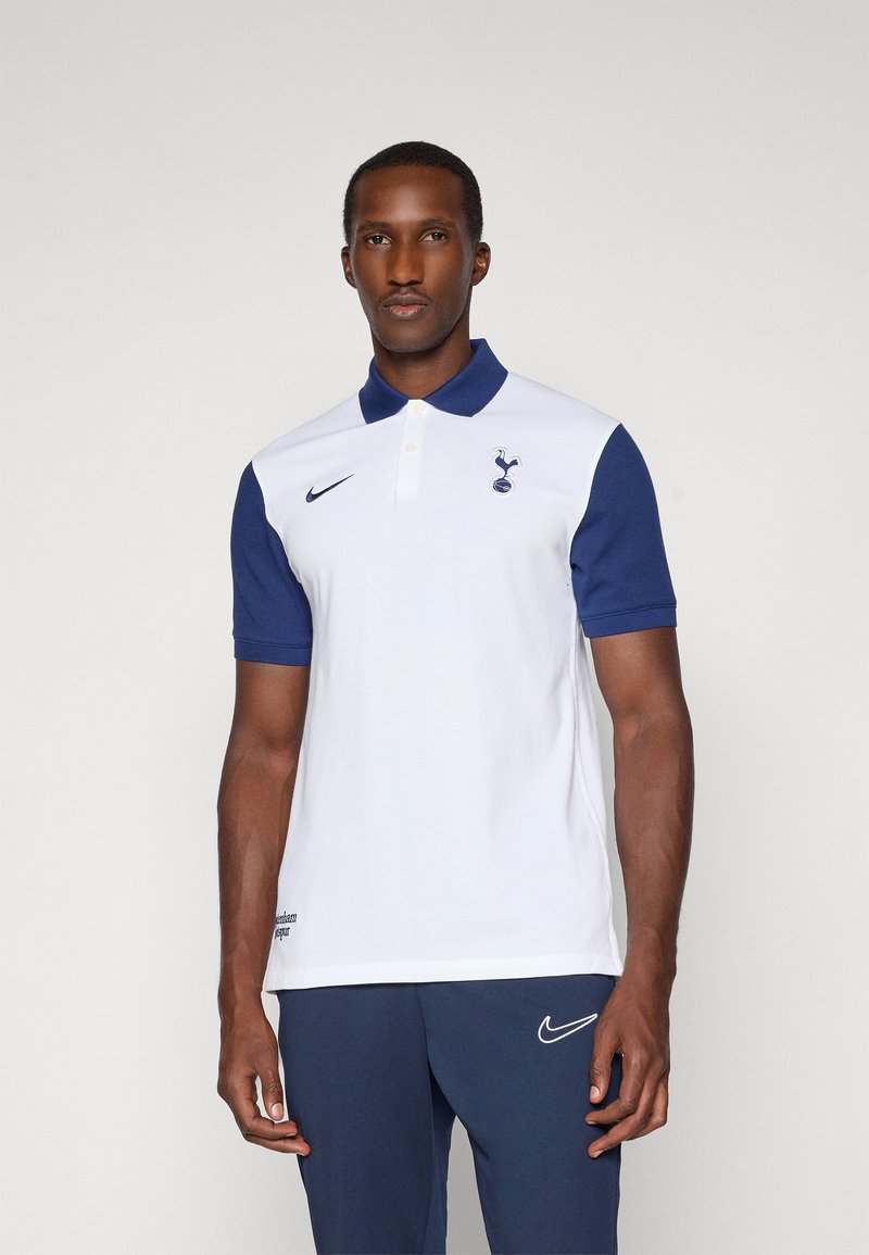 Polo shirt blanc avec des accents bleu marine, doté d'un col, de trois boutons et d'un logo de Tottenham Hotspur. Fabriqué en mélange de coton lisse.
