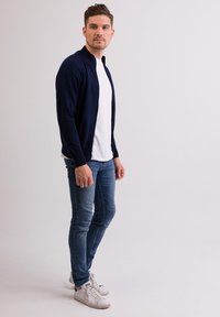 Granatowy kardigan z kołnierzykiem, założony na biały T-shirt. Dopasowane niebieskie dżinsy i białe sneakersy dopełniają casualowy wygląd.