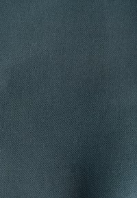 Tejido en tono verde azulado con una textura suave y un ligero brillo. Presenta un patrón tejido diagonal que crea un sutil y elegante detalle en la superficie.
