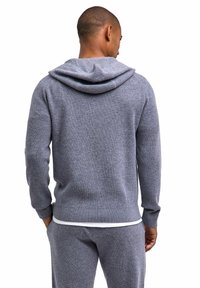 Grauer Kapuzenpullover aus Strick mit geripptem Muster, ausgestattet mit einem Kordelzug an der Kapuze und Bündchen an den Ärmeln, kombiniert mit passenden grauen Hosen.