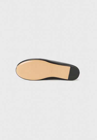 Suela de zapato de cuero negro con una superficie lisa, con una plantilla beige y una ligera curva en la punta. Diseño minimalista sin patrones visibles.