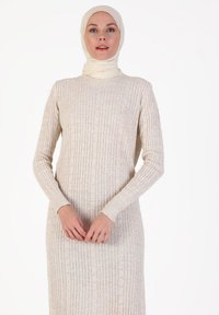 Robe en tricot côtelé beige à manches longues, col rond et motif texturé. Le mannequin porte un foulard assorti.