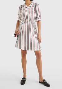 Kortärmad knapparklänning med röda och svarta vertikala ränder på vit bakgrund, som har dragsko i midjan och avslappnad passform.