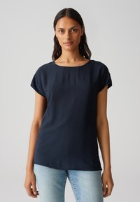 Top blu navy a maniche corte con scollo rotondo e tessuto morbido e fluido. Indossato con jeans azzurri.