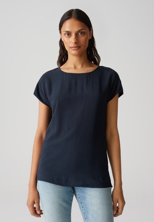 Haut à manches courtes bleu marine avec un col rond et un tissu lisse et fluide. Porté avec un pantalon en jean bleu clair.