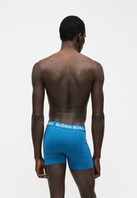 Άνδρας μοντέλο, εμφανιζόμενος από πίσω, που φοράει μπλε μπόξερ Björn Borg σε λευκό απλό φόντο.