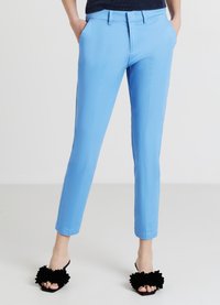 Hellblaue, maßgeschneiderte Hose mit seitlichen Taschen, flacher Vorderseite und knöchellanger Passform. Getragen mit schwarzen Pantoletten mit floralen Akzenten.