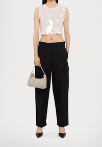 Valkoinen paljetti cropped-top, jossa on hapsureunus, yhdistetty mustiin cargo-housuihin, joissa on sivutaskut, ja sen kanssa pieni teksturoitu käsilaukku.