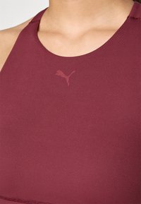 Bordo sportski gornji dio s udubljenim izrezom, izrađen od glatkog materijala. Sadrži suptilan Puma logo u nešto tamnijoj nijansi.