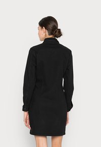 Vestido de ganga preto com mangas longas, punhos abotoados e colarinho estruturado. Silhueta ajustada e design minimalista sem padrões.