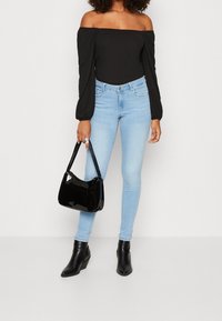 Musta olkaimeton paita, vaaleansiniset skinny-farkut, musta lakattu käsilaukku ja mustat nilkkurit. Tasainen pinta, istuva muotoilu ja tyylikäs siluetti.