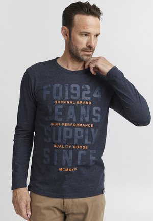 Camiseta de manga larga de color navy con textura moteada, que presenta un diseño de texto en negro y naranja en negrita. Cuello redondo y ajuste regular.
