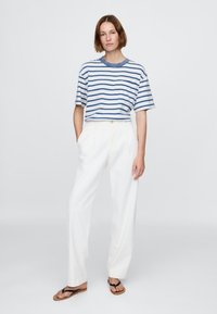 Stripet T-skjorte med korte ermer i blått og hvitt, kombinert med hvite bukser med vide ben. Fottøyet består av svarte flip-flops med flate såler.