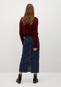 Pitkä farkkuhame, jossa on takarako, yhdistettynä punaiseen neulepuseroon. Mustat nilkkurit täydentävät asua. Sileä pinta ja klassinen leikkaus.