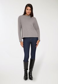 Szary sweter z długim rękawem i okrągłym dekoltem, w połączeniu z ciemnoniebieskimi rurkami i czarnymi skórzanymi kozakami do kolan.