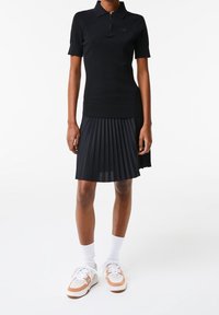 Černý polokošile s krátkými rukávy má zipový límec a žebrovaný vzor. Kombinováno s plisovanou černou sukní a bílými teniskami s akcenty.