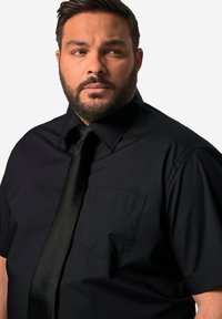 Svart kortärmad skjorta med standardkrage och vänster bröstficka, kombinerad med en svart slips. Slätt material, enhetlig färg, klassisk design.