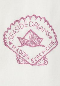 Coquillage rose brodé avec un bateau en papier au centre et le texte "SEASIDE DREAMS" et "MADEIRA BEACH CLUB" sur tissu blanc.