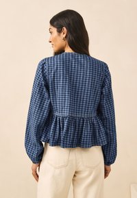 Plava bluza s gingham uzorkom dugih rukava, s peplum rubom i naborima u području struka. Mekani materijal sa teksturiranim izgledom.