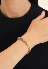Pulsera de eslabones de metal dorado y plateado con formas rectangulares alternas, con un acabado pulido y textura suave.