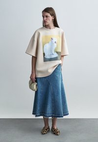 Μπεζ ανοιχτό φούτερ με γραφικό γάτας, σε συνδυασμό με φούστα από τζιν με καμπάνες στο τελείωμα και σκισμένες άκρες, και παπούτσια με λεοπάρ λεπτομέρειες.