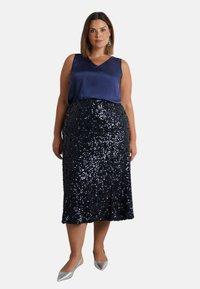 Námořnický saténový top bez rukávů doplněný černou sukni ke kolenům zdobenou flitry. Outfit doplňují stříbrné špičaté baleríny.