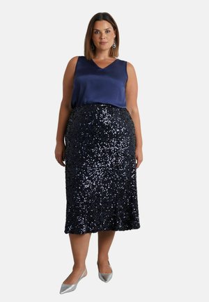 Marineblauwe satijnen mouwloze top gecombineerd met een knielange zwarte paillettenrok. Zilverkleurige puntige instappers maken de outfit compleet.