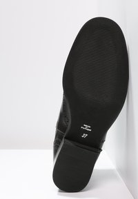 Černá kožená podrážka s ribbovanou texturou, s velikostí 37 a nápisem "Vyrobeno v Portugalsku". Čistý design bez dalších ozdob.