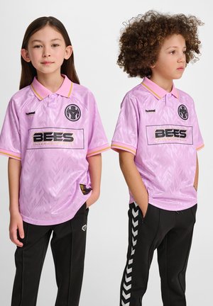 Roze sportshirts hebben een geometrisch patroon, een kraag en branding. Deze zijn gecombineerd met zwarte broeken met een wit zigzagpatroon.