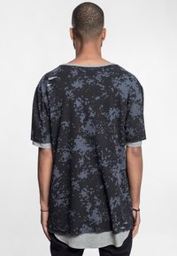 Sort t-shirt med et sprøjt mønster i varierende nuancer af grå. Løs pasform med vid halsudskæring og korte ærmer, lagdelt med gråt stof nedenunder.