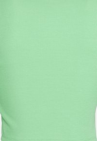 Närbild av ljusgrön ribbad textil med subtil vertikal struktur och en söm i nederkant.