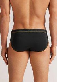 Svarta herrunderkläder med en olivgrön midjeband och sömmar. Designen har en mjuk yta och en åtsittande passform.