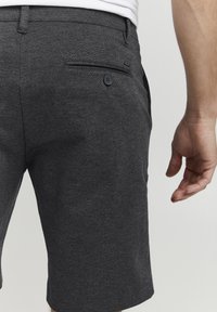 Shorts ajustés gris foncé en tissu texturé, avec une poche arrière à fermeture boutonnée et des détails de couture subtils.