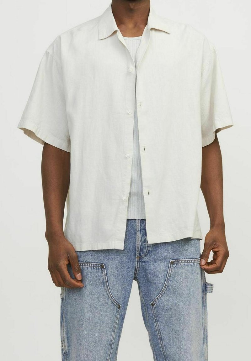Lichtbeige, kortärmelig overhemd met knopen, gemaakt van een gestructureerde stof, voorzien van een verspreide kraag en een ontspannen pasvorm. Gecombineerd met blauwe spijkerbroek.