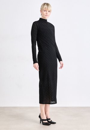 Black long-sleeve midi dress with a high neckline, featuring a patterned, sheer fabric. Paired with black high-heeled shoes.