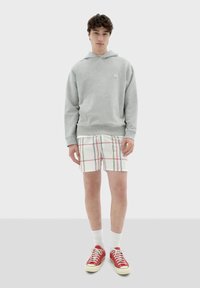 Grijze fleece hoodie, witte en geruite shorts met rode, groene en blauwe lijnen, rode sneakers en witte sokken. Eenvoudig ontwerp, casual pasvorm.