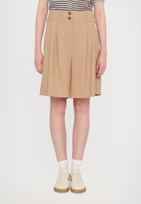 Beige tailored shorts with pleats and two front buttons. Worn with a striped shirt and light-colored shoes, presenting a relaxed fit.
