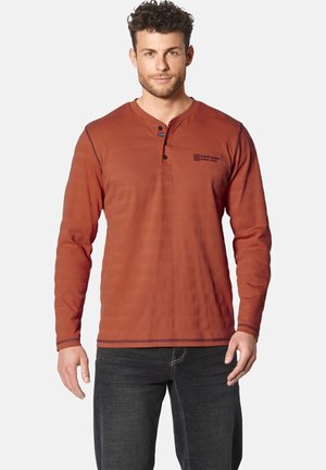 Long-sleeve rust-colored henley shirt with textured stripes, two buttons at the neckline, and contrasting navy stitching details.