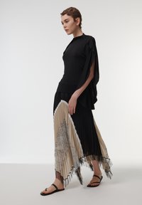 Top negro ajustado con mangas acampanadas, falda de capas con pliegues en negro y beige, con un patrón, y sandalias planas negras.
