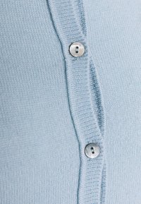 Ljusblå cardigan med en strukturerad stickning, som har fyra runda, ljusa knappar framtill och en ribbad kant.