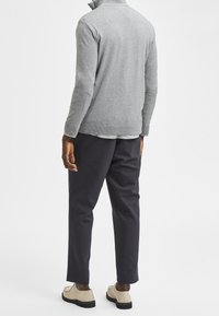 Grå tröja med hög krage, kombinerad med marinblå byxor och beige skor. Strukturerad stickning och ribbade muddarna förbättrar utseendet.