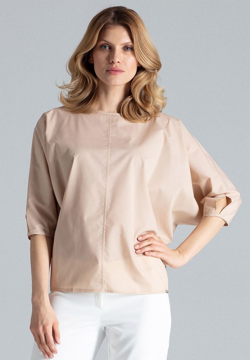 Beżowa, oversize bluzka z rękawami do łokci, minimalistyczny design i gładka tekstura; posiada centralnie umieszczony detal w postaci ściegu.