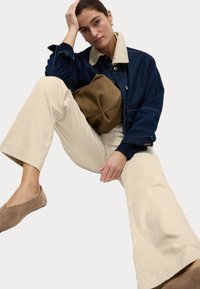 Jeansjacka med en beige krage, krämfärgade vida byxor och taupefärgade lägenheter. En brun väska hålls i ena handen. Släta tygtexturer.