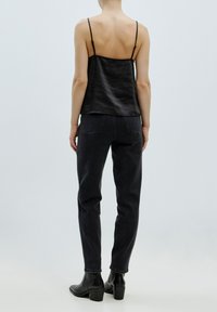 Zwart satijnen camisole met dunne bandjes, gecombineerd met hoge zwarte spijkerbroek. Model draagt enkellaarsjes met een blokhak.