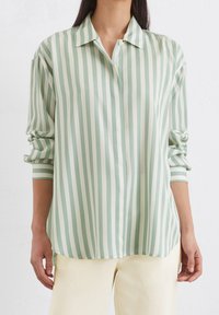 Camicia a righe verde chiaro e bianca con colletto, chiusura a bottoni e maniche arrotolate, realizzata in un materiale liscio. Presenta una vestibilità rilassata.