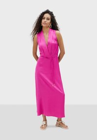 Vestido sin mangas en fucsia con escote en V profundo, lazo en la cintura y longitud maxi fluida. Tela suave con un brillo sutil.