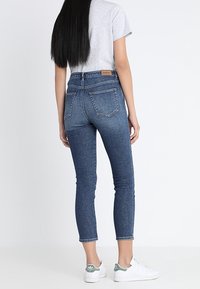 Högmidjade blå denimjeans med slim fit, med femfickorsdesign och subtila sömmar, kombinerade med vita sneakers.