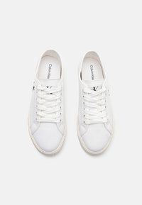 Białe płócienne sneakersy z teksturowanym wykończeniem, z sznurowadłami i logo na języku. Gumowe podeszwy z okrągłym wzorem bieżnika.