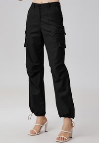 Pantalons cargo noirs avec une coupe fuselée, dotés de plusieurs poches latérales, de poignets à cordon de serrage et d'un tissu lisse et texturé.